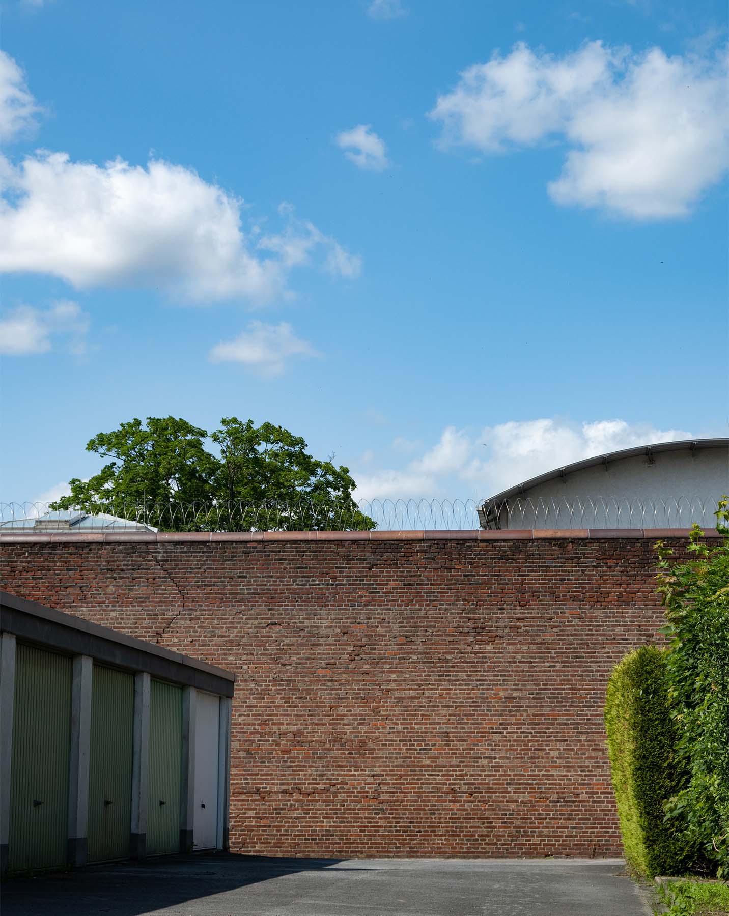 Blick auf die mit stacheldraht versehene Aussenmauer einer JVA. Ein sonniger Tag.